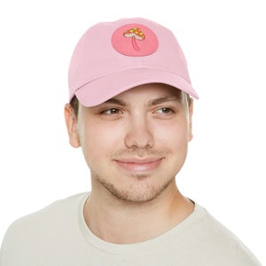 May include: A pink baseball cap with a mushroom patch. The mushroom is yellow and red with white spots.