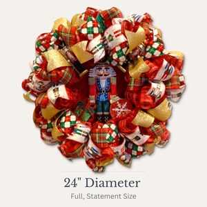 Puede incluir: Una festiva corona navide&ntilde;a, de 61 cm de di&aacute;metro, con una figura central de cascanueces. La corona est&aacute; adornada con cintas rojas, verdes y doradas, y detalles de cuadros escoceses, creando una decoraci&oacute;n navide&ntilde;a completa y llamativa.