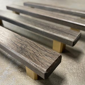 May include: Four wooden cabinet pulls with a textured, gray-brown finish. Each pull is rectangular with rounded edges and is mounted on a small, light-colored wooden block. The pulls are arranged in a row, slightly angled.