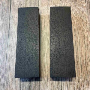 May include: Two dark grey wood blanks, each approximately 25 cm long and 5 cm wide. The wood has a unique grain pattern.