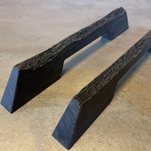 Könnte beinhalten: Zwei schwarze Holzknaufgriffe mit einer rauen, strukturierten Oberfläche. Die Griffe haben eine rechteckige Form mit einem Ausschnitt in der Mitte für einen Griff.