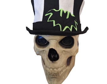 May include: A white and black striped top hat with a green bat design on the front. The hat is sitting on a white skull.