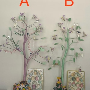 May include: Two decorative Easter trees with pastel-colored branches, leaves, and flowers. One tree is purple, the other is green. Each tree has a decorative base with figurines and a framed display of Easter eggs. The letter "A" and "B" are above the trees.