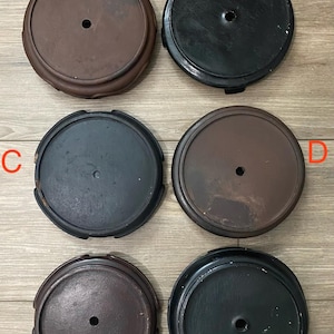 May include: A collection of six wooden display stands in various shades of brown and black. Each stand is round with a central hole, and some have decorative edges. The stands are likely for displaying small sculptures or collectibles.