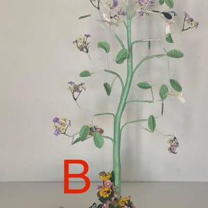 May include: A decorative tree sculpture with a light green trunk, silver branches, and small birds perched on the branches. The tree has green leaves and clusters of purple and yellow flowers. A yellow box with a floral design is in the foreground.