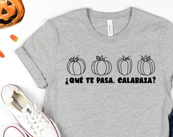 Puede incluir: Una camiseta gris con un gráfico negro de cuatro calabazas y el texto "¿Qué te pasa, calabaza?" en español.