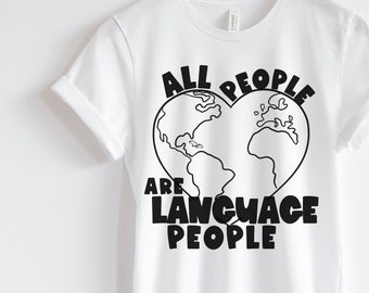 Può includere: Maglietta bianca con un design grafico nero. La grafica presenta un contorno a forma di cuore del mondo con il testo "All People Are Language People".