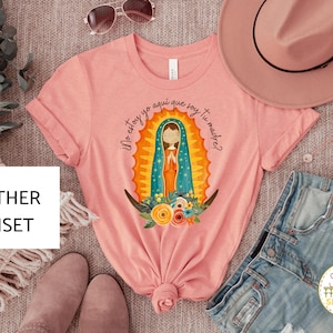 Puede incluir: Una camiseta rosa con un gr&aacute;fico de la Virgen Mar&iacute;a en una t&uacute;nica azul y dorada. El texto "Yo estoy yo aqui que soy tu madre?" est&aacute; impreso en la camiseta.