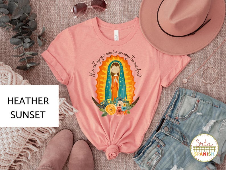 Puede incluir: Una camiseta rosa con un gr&aacute;fico de la Virgen Mar&iacute;a en una t&uacute;nica azul y dorada. El texto "Yo estoy yo aqui que soy tu madre?" est&aacute; impreso en la camiseta.