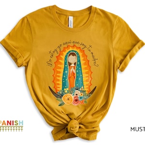 Puede incluir: Camiseta amarilla mostaza con un gr&aacute;fico de la Virgen Mar&iacute;a con una t&uacute;nica azul y dorada. El texto "No estoy yo aqu&iacute; que soy tu madre?" est&aacute; impreso en la camiseta.
