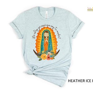 Puede incluir: Una camiseta azul claro con un gr&aacute;fico de la Virgen Mar&iacute;a en un marco dorado y azul. El texto "&iexcl;No estoy yo aqu&iacute; que soy tu madre?" est&aacute; impreso en la camiseta.