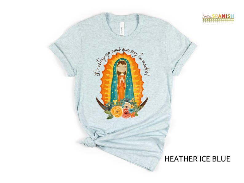 Puede incluir: Una camiseta azul claro con un gr&aacute;fico de la Virgen Mar&iacute;a en un marco dorado y azul. El texto "&iexcl;No estoy yo aqu&iacute; que soy tu madre?" est&aacute; impreso en la camiseta.