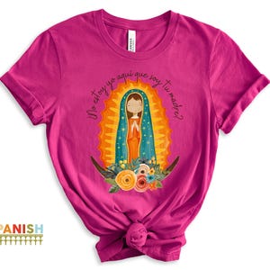 Puede incluir: Una camiseta rosa con un gr&aacute;fico de la Virgen Mar&iacute;a en un marco dorado. El texto "No estoy yo aqu&iacute; que soy tu madre?" est&aacute; impreso en la camiseta.