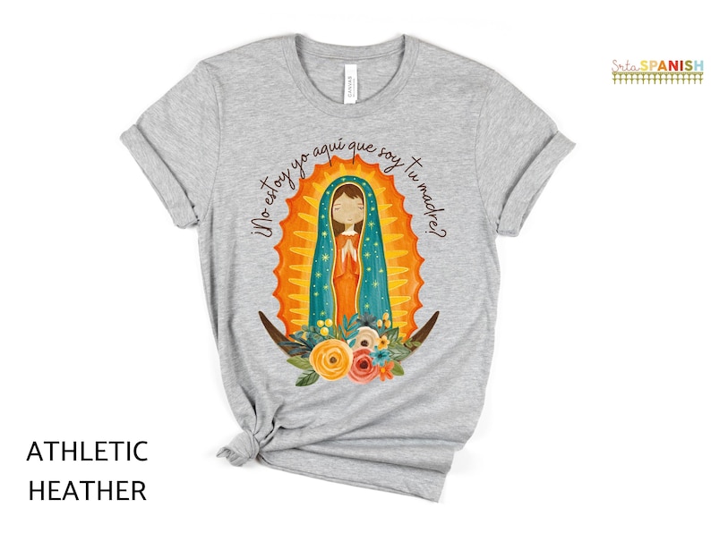 Puede incluir: Una camiseta gris jaspeada con un gr&aacute;fico de la Virgen Mar&iacute;a en una t&uacute;nica azul y dorada. El texto "&iexcl;No estoy yo aqu&iacute; que soy tu madre?" est&aacute; impreso en la camiseta.