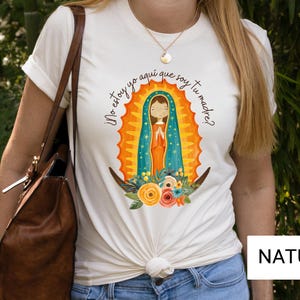 Puede incluir: Camiseta blanca con una ilustraci&oacute;n colorida de la Virgen Mar&iacute;a. El texto en la camiseta dice "&iexcl;No estoy yo aqu&iacute; que soy tu madre?"