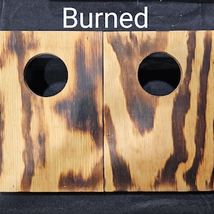 May include: Two wooden boards with circular cutouts, both showing signs of burning and charring. The boards are light brown with dark brown streaks and patches.