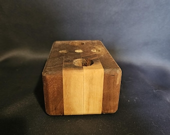May include: A rectangular wooden block with three holes on top. The block is made of different wood tones, with a light-colored stripe down the center and darker wood on the sides. The object is likely a desk organizer or pen holder.