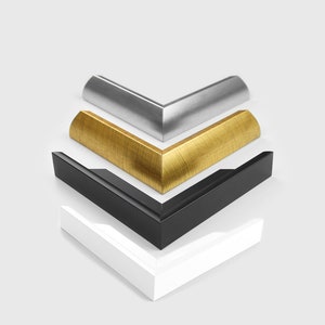 May include: Four picture frame corners in different colors: white, black, gold, and silver. The corners are stacked on top of each other.