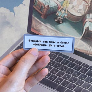 Op de afbeelding: Een rechthoekige sticker met de tekst "Computer can have a little shutdown. As a treat." in zwarte letters. De sticker wordt voor een laptop gehouden.