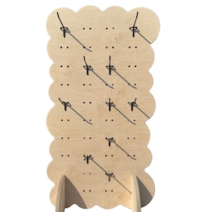 May include: A wooden display stand with a cloud-shaped design. The stand is made of light-coloured wood and features multiple hooks for hanging items. It has two supporting legs at the base. The stand is designed to showcase merchandise.