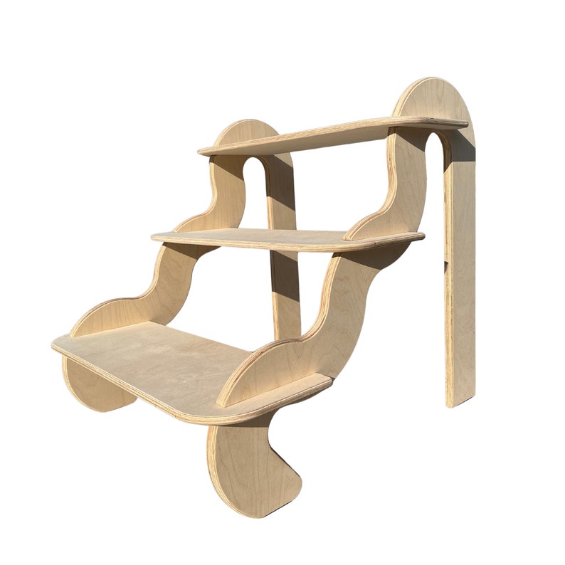 May include: A three-tiered wooden shelf unit with a unique, wavy design. The shelves are made of natural wood and have a light brown finish. The unit is freestanding and has a modern, minimalist aesthetic.