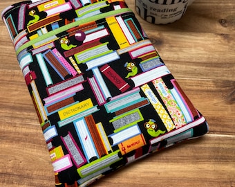 Puede incluir: Una funda de libro negra con un patrón colorido de libros apilados. Los libros tienen títulos como "Geografía", "Ciencia", "Biología", "Diccionario" y "El Mundo". También hay pequeños gusanos verdes con gafas en la funda.