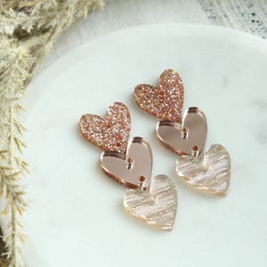 May include: Rose gold heart shaped earrings with glitter and a textured design.