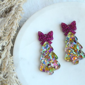 May include: A pair of iridescent glitter Christmas tree earrings with pink glitter bows.