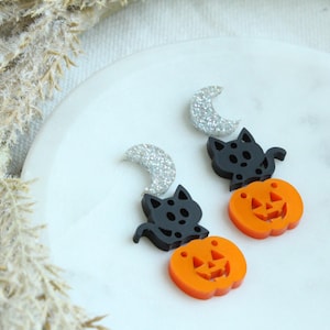 May include: A pair of Halloween-themed earrings featuring black cat and orange pumpkin charms with silver glitter crescent moons.