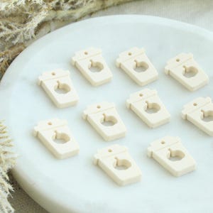 May include: Ten cream-colored wooden coffee cup charms with a pumpkin cutout. The charms are arranged in two rows of five on a white surface.