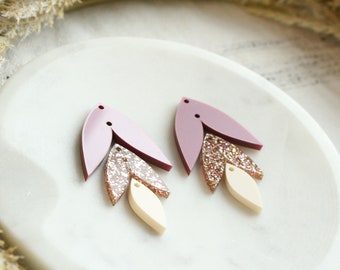 May include: A pair of pink and cream layered dangle earrings with a glitter accent. The earrings are made of acrylic and have a simple, modern design.