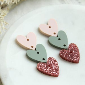 May include: Three layered heart shaped charms in pink, green, and glitter pink. Each heart has a hole in the center.