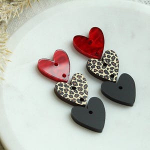 May include: Three heart-shaped buttons in a stack. The top button is red, the middle button is brown with a leopard print, and the bottom button is black.