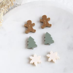May include: A set of six Christmas-themed earrings featuring gingerbread men, Christmas trees, and snowflakes. The gingerbread men are gold, the trees are green, and the snowflakes are white.