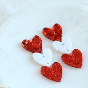 May include: Three red glitter heart-shaped charms with white heart-shaped charms in between.