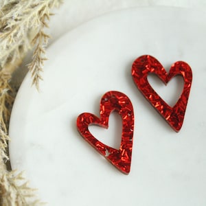 May include: Two red glitter heart-shaped earrings with a cutout design.
