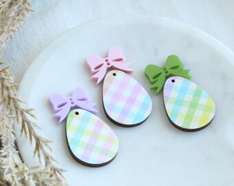 May include: Three pastel Easter egg shaped ornaments with gingham patterns and bows. The ornaments are pink, green, and purple.