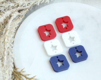 Op de afbeelding: Zes vierkante acrylcharms met een stervormige uitsparing. Twee rode, twee witte en twee blauwe charms.