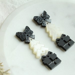 May include: Two black and white Christmas tree ornaments with glitter. Each ornament features a black bow, a white Christmas tree, and a black gift box.