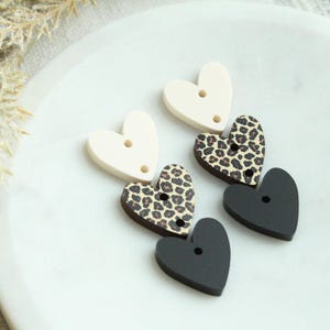 May include: Three heart-shaped buttons in black, white, and leopard print. The buttons have two holes each.