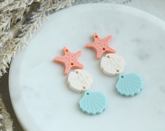 May include: A pair of earrings featuring a pink starfish, a white seashell, and a light blue seashell charm.
