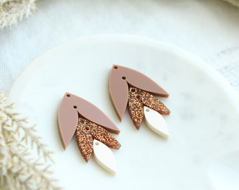 May include: A pair of dangle earrings with a layered design. The top layer is a brown teardrop shape, the middle layer is a gold glitter teardrop shape, and the bottom layer is a white teardrop shape.