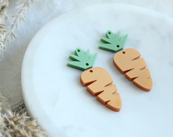May include: Two orange carrot shaped earrings with green leafy tops. The earrings are made of acrylic and have a hole for a hook.