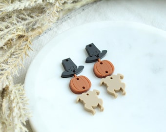 May include: Two pairs of fall-themed earrings. Each pair features a black pilgrim hat charm, a brown pumpkin charm, and a tan turkey charm.