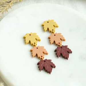 May include: Five maple leaf shaped charms in various shades of fall colors. The charms are made of resin and have two holes for attaching to jewelry or other crafts.