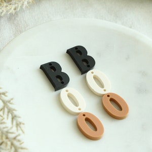 May include: A pair of black and brown Halloween earrings with the word "BOO" spelled out in acrylic letters.