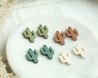 May include: Seven cactus-shaped charms in various shades of green, brown, and cream. The charms are made of a smooth, rubber-like material and have a hole at the top for hanging.