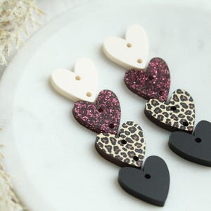 May include: A set of six heart-shaped buttons in various patterns. The buttons are white, pink glitter, leopard print, and black. Each button has two holes for sewing.