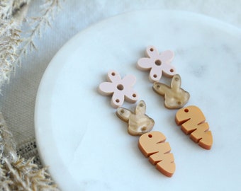 May include: A set of six acrylic earrings in pastel pink and orange. The earrings are shaped like flowers, carrots, and bunnies.