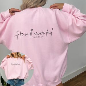 Puede incluir: Sudadera rosa con el texto "He will never fail" y "PSALMS 46:5" en la espalda. La parte delantera de la sudadera tiene el texto "Trust in God".